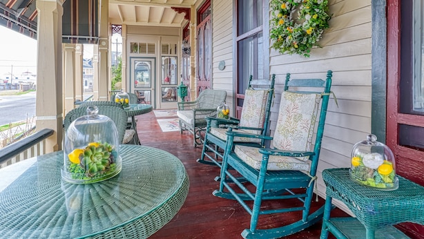 A porch with wicker furniture, a covered table with a plant, and a decorative wreath. - Bedford Inn (Cape May)