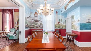 A dining room with a long wooden table, red walls, and maritime-themed murals. - Bedford Inn (Cape May)