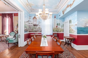 A dining room with a long wooden table, red walls, and maritime-themed murals.