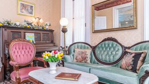 A room with a green sofa, a pink chair, a wooden desk, and a lamp. - Bedford Inn (Cape May)