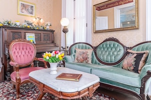 A room with a green sofa, a pink chair, a wooden desk, and a lamp.