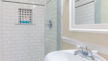 A bathroom with white tiled walls, a glass shower enclosure, and a white sink with chrome fixtures.