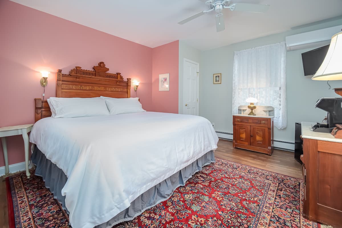 A bedroom with a large bed, a wooden headboard, a nightstand, a desk, a chair, a desk lamp, a television, and a patterned rug.