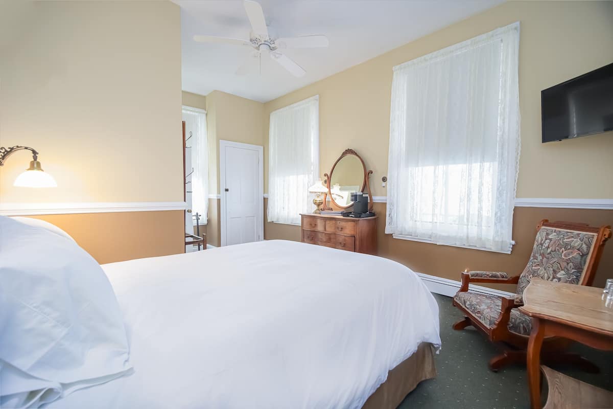 A hotel room with a large bed, a desk, a chair, a dresser, a mirror, and a ceiling fan.