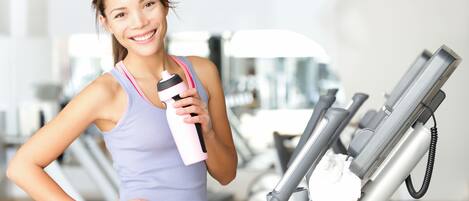 A person in a gym holding a water bottle and standing next to a treadmill.
