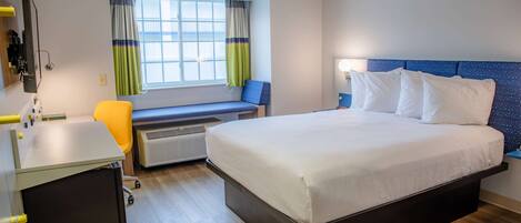 Una habitación de hotel con cama, escritorio, silla, ventana con cortinas y un calefactor.