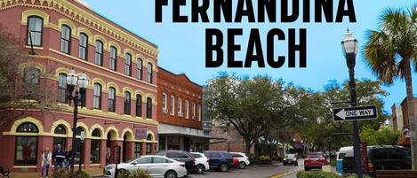 A street view of Fernandina Beach with historic buildings, parked cars, and a 'One Way' sign.