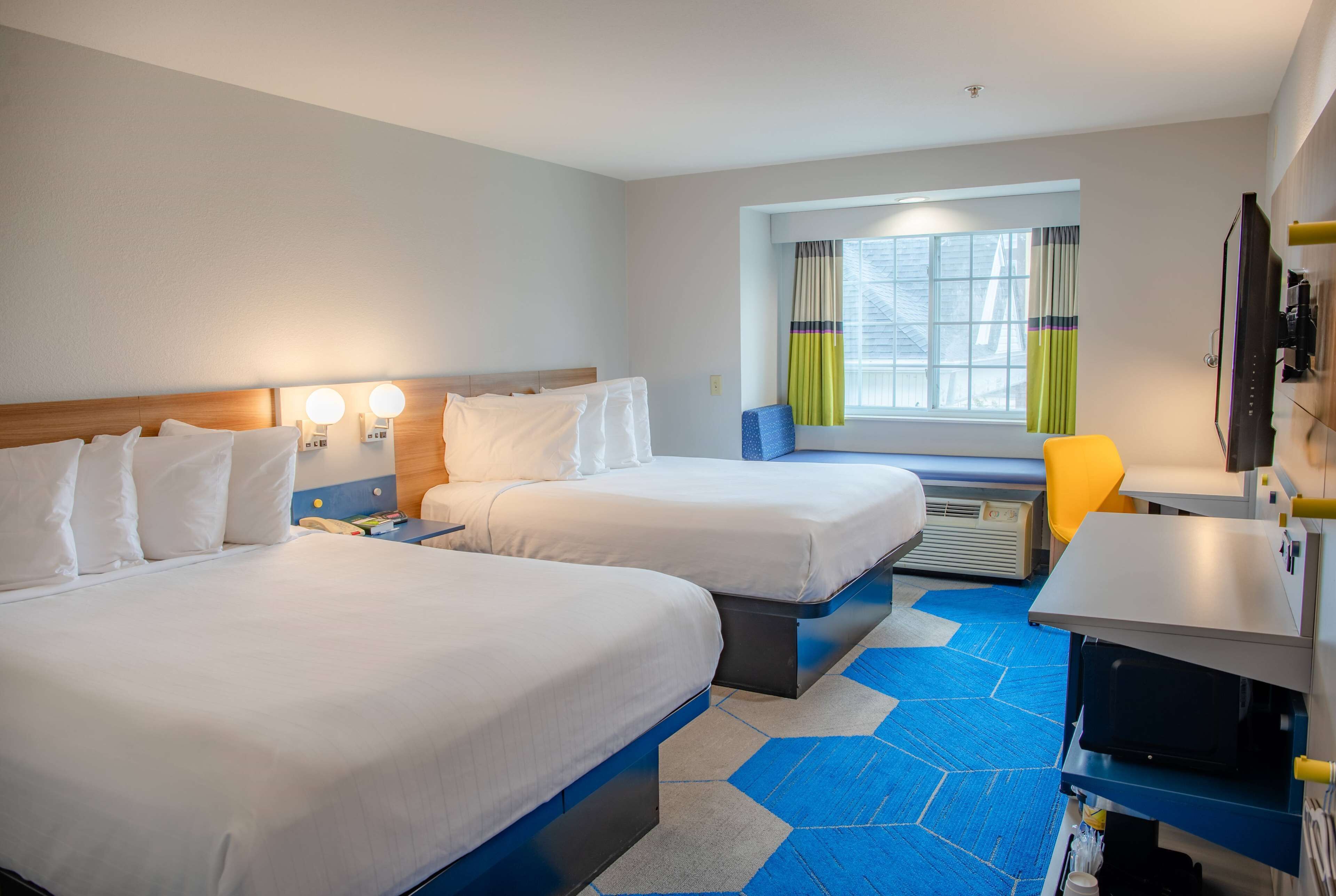 Habitación de hotel con dos camas, un escritorio, una silla, un microondas y una ventana con cortinas.