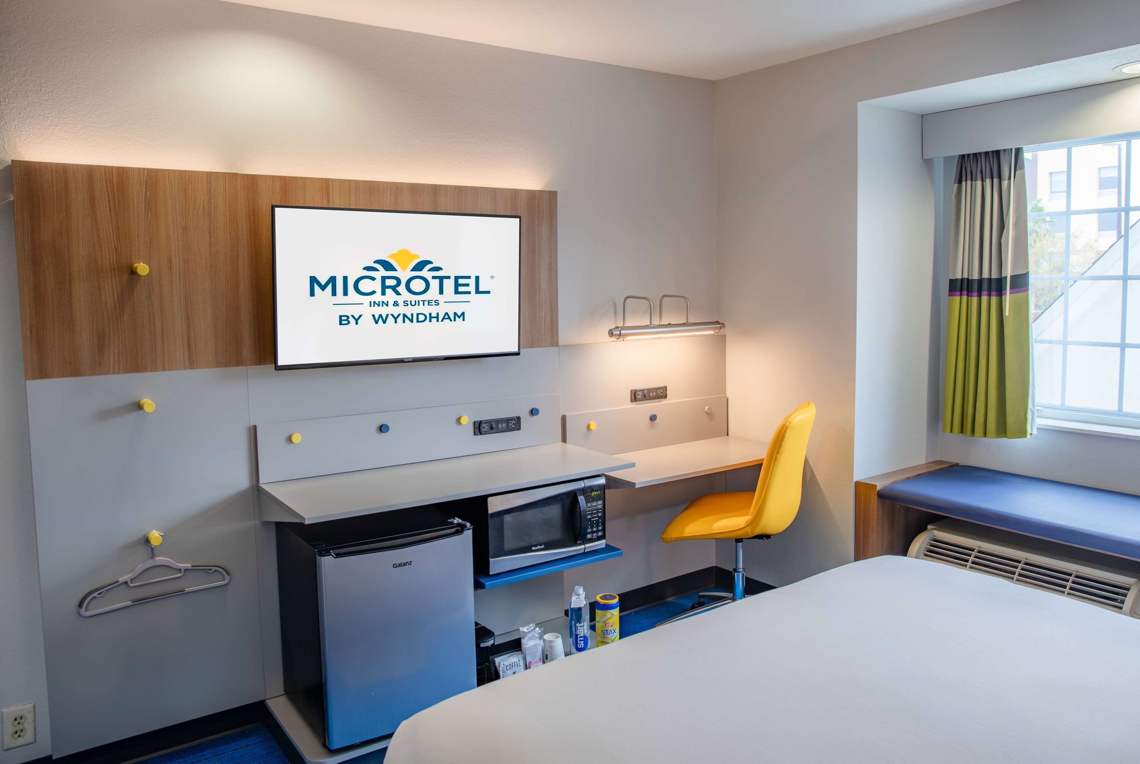 A compact hotel room with a kitchenette, a bed, a desk, and a chair.