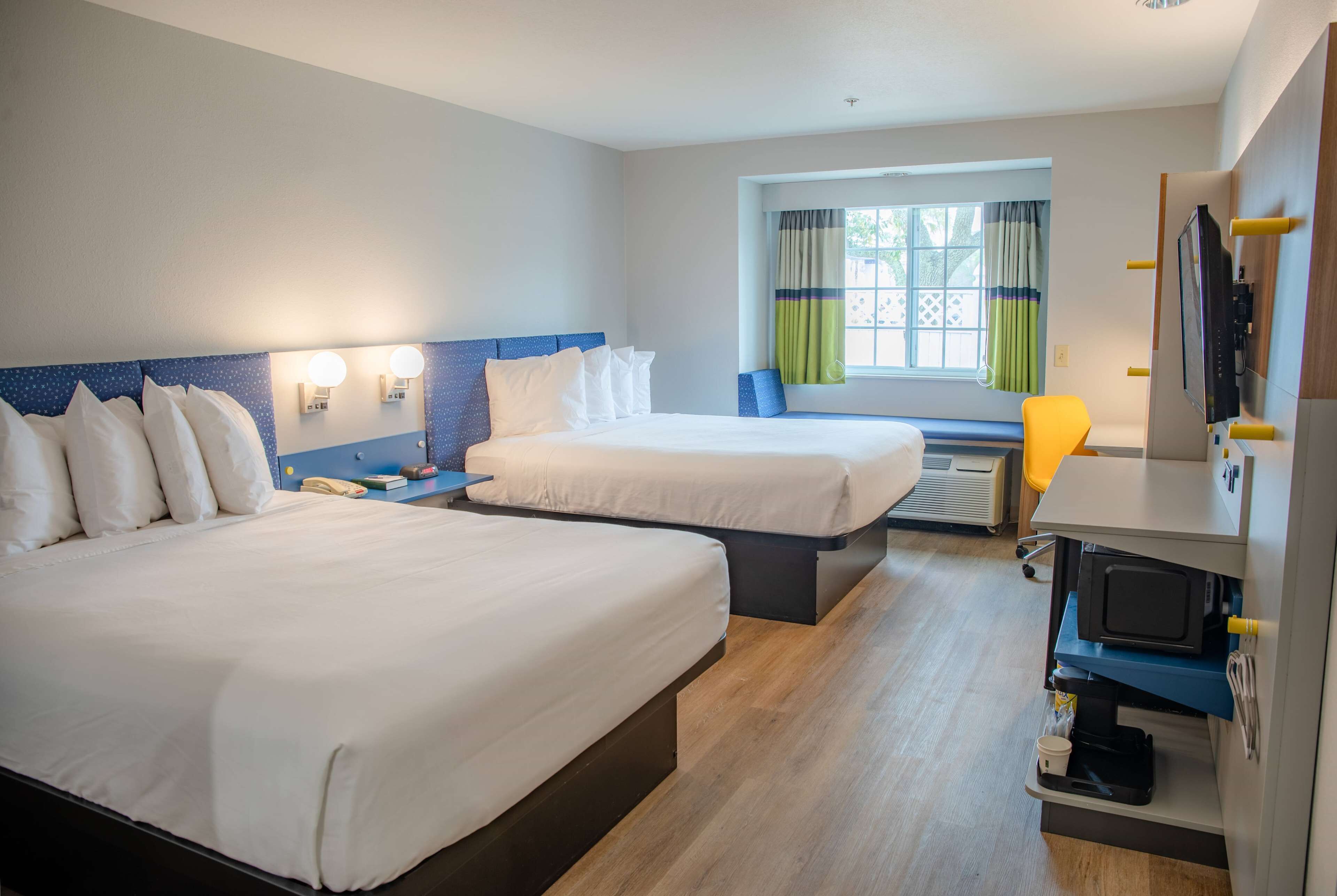 A hotel room with two beds, a TV, a coffee machine, and a window with curtains.