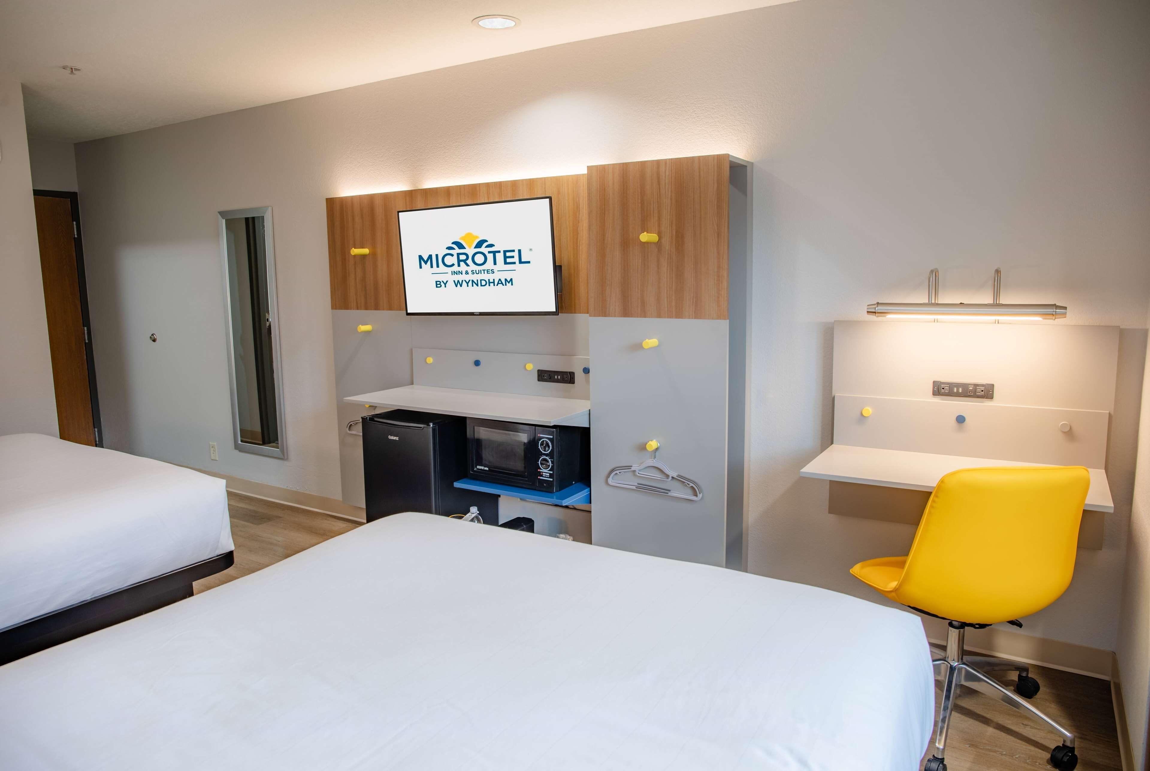Een hotelkamer met twee bedden, een bureau met een computer, een magnetron en een televisie waarop het logo van Microtel Inn & Suites te zien is.
