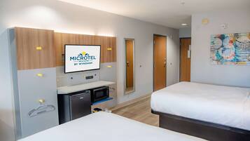 A hotel room with a bed, a desk with a microwave, a small fridge, and a TV displaying the hotel's logo.