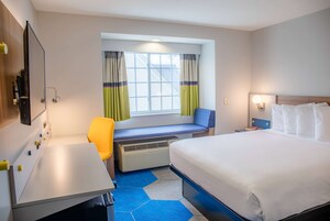 Habitación de hotel con una cama grande, un escritorio, una silla, una ventana con cortinas y vistas al exterior.