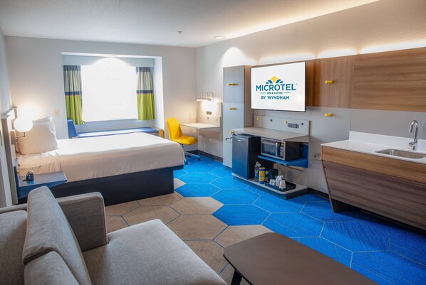 Habitación de hotel con cama, escritorio, silla, televisor, microondas, lavamanos y minibar.