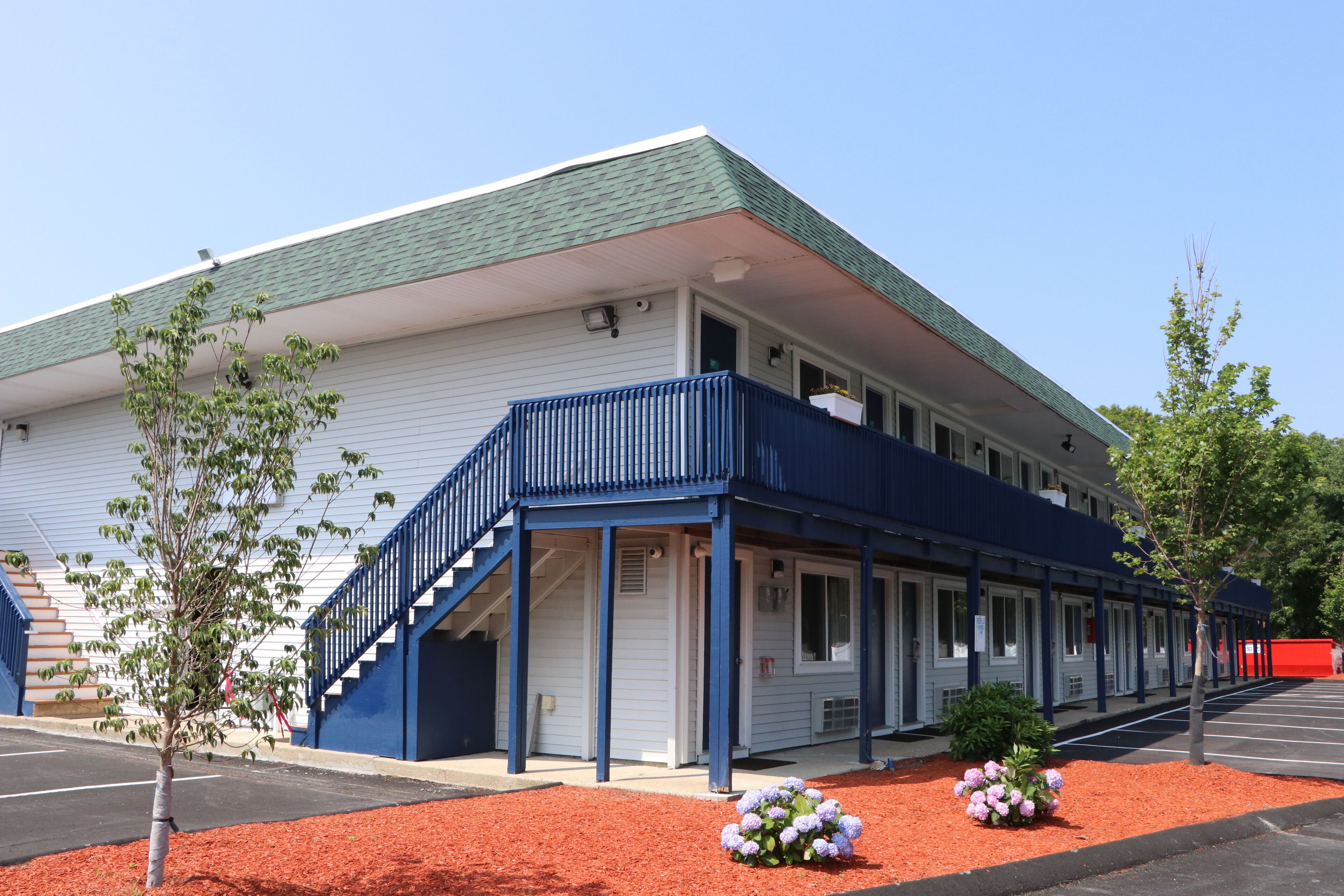 A motel with a blue exterior, a covered front porch, and a parking lot.
