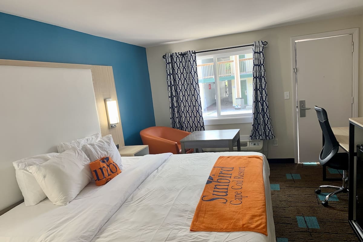 Une chambre d’hôtel avec un lit, un bureau, une chaise et une fenêtre agrémentée de rideaux à motifs.