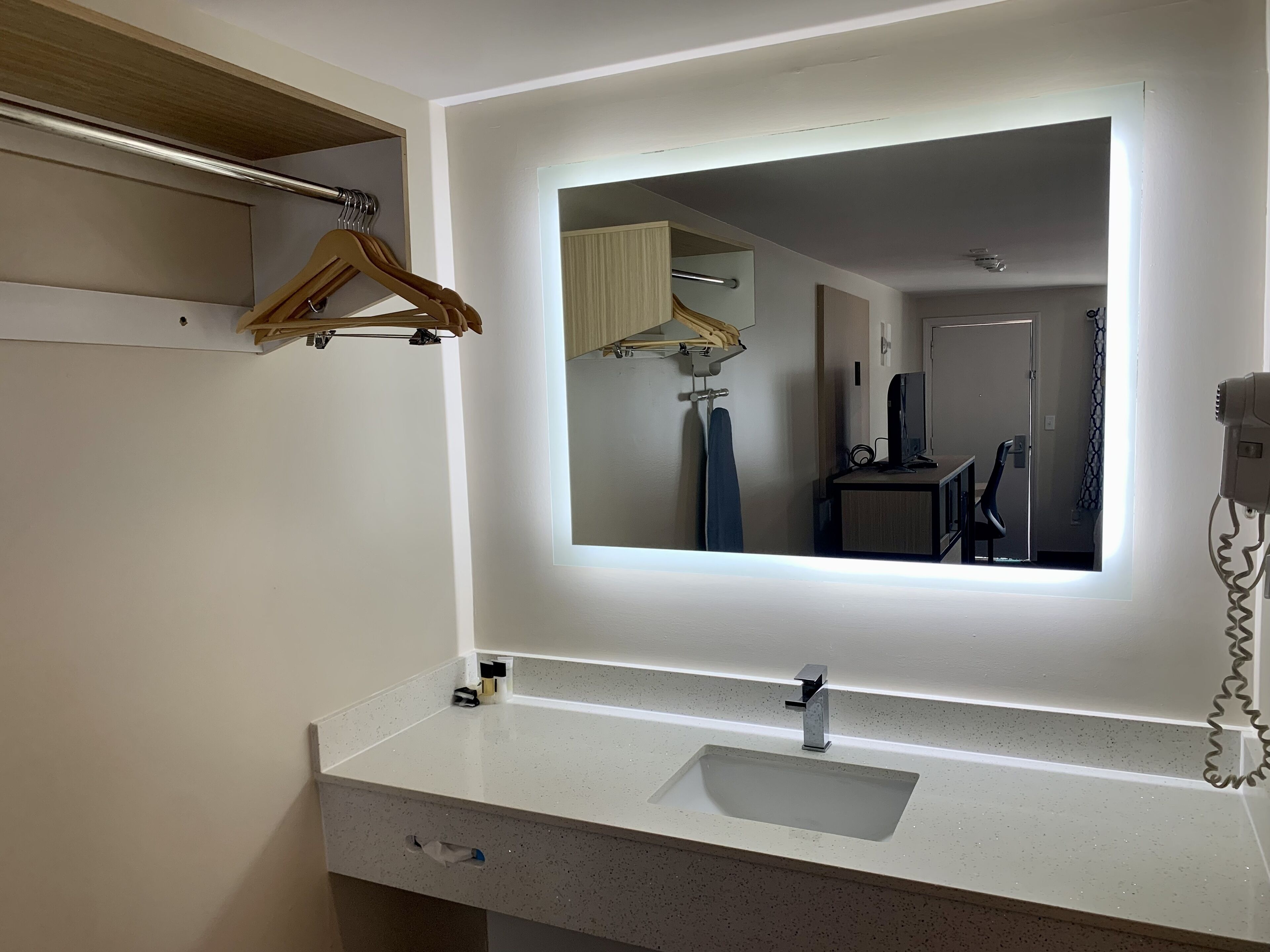 A bathroom with a large mirror, a sink, a towel rack, and a hairdryer.