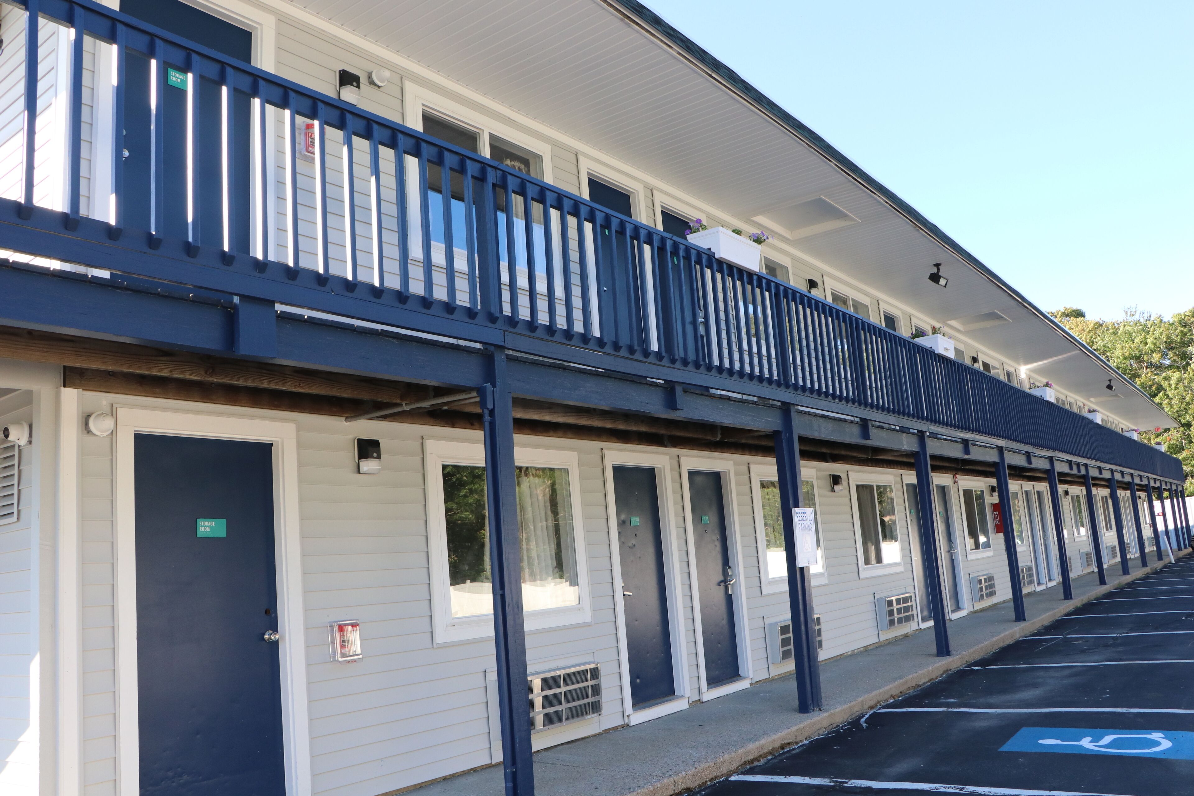 Un motel con galería techada, habitaciones individuales y estacionamiento.