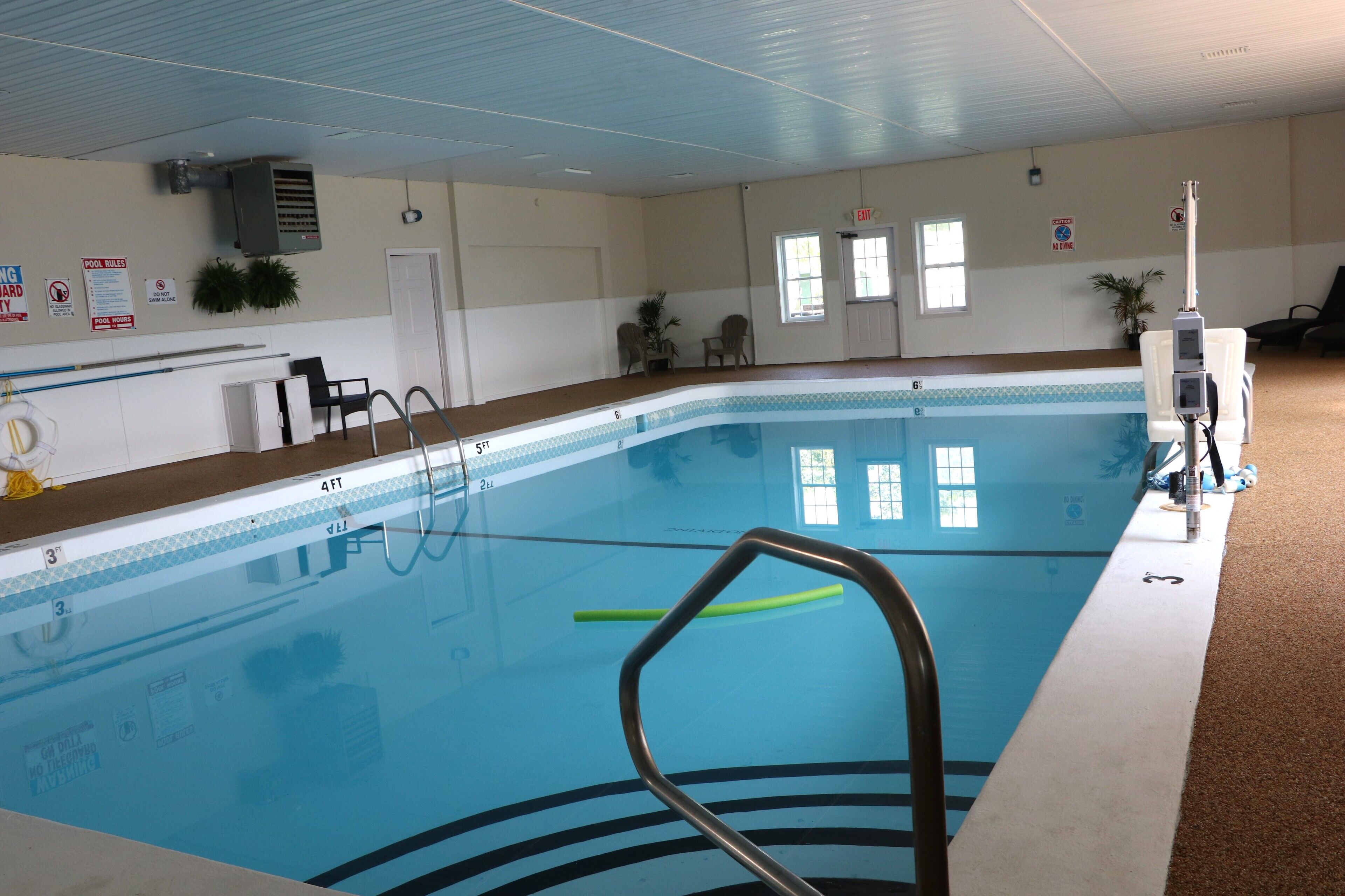 An indoor swimming pool with clear water, marked depth lines, and a lifeguard chair.