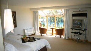 A hotel room with a large bed, a TV, a small table, two chairs, and a window with a view of greenery. - Las Ramblas de Puerto Manzano (Villa La Angostura)