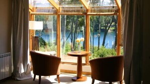 A room with a large window, two chairs, a small table with a vase, and a lamp. - Las Ramblas de Puerto Manzano (Villa La Angostura)