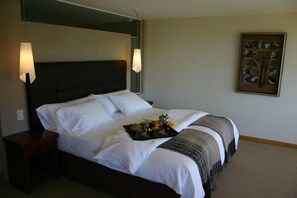 A neatly made bed with white linens, a tray of fruit, and a framed picture on the wall.