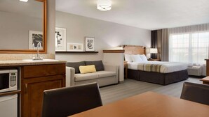 A hotel room with a kitchenette, a bed, a sofa, a dining table, and a large mirror. - Country Inn & Suites by Radisson, Appleton North, WI (Little Chute)