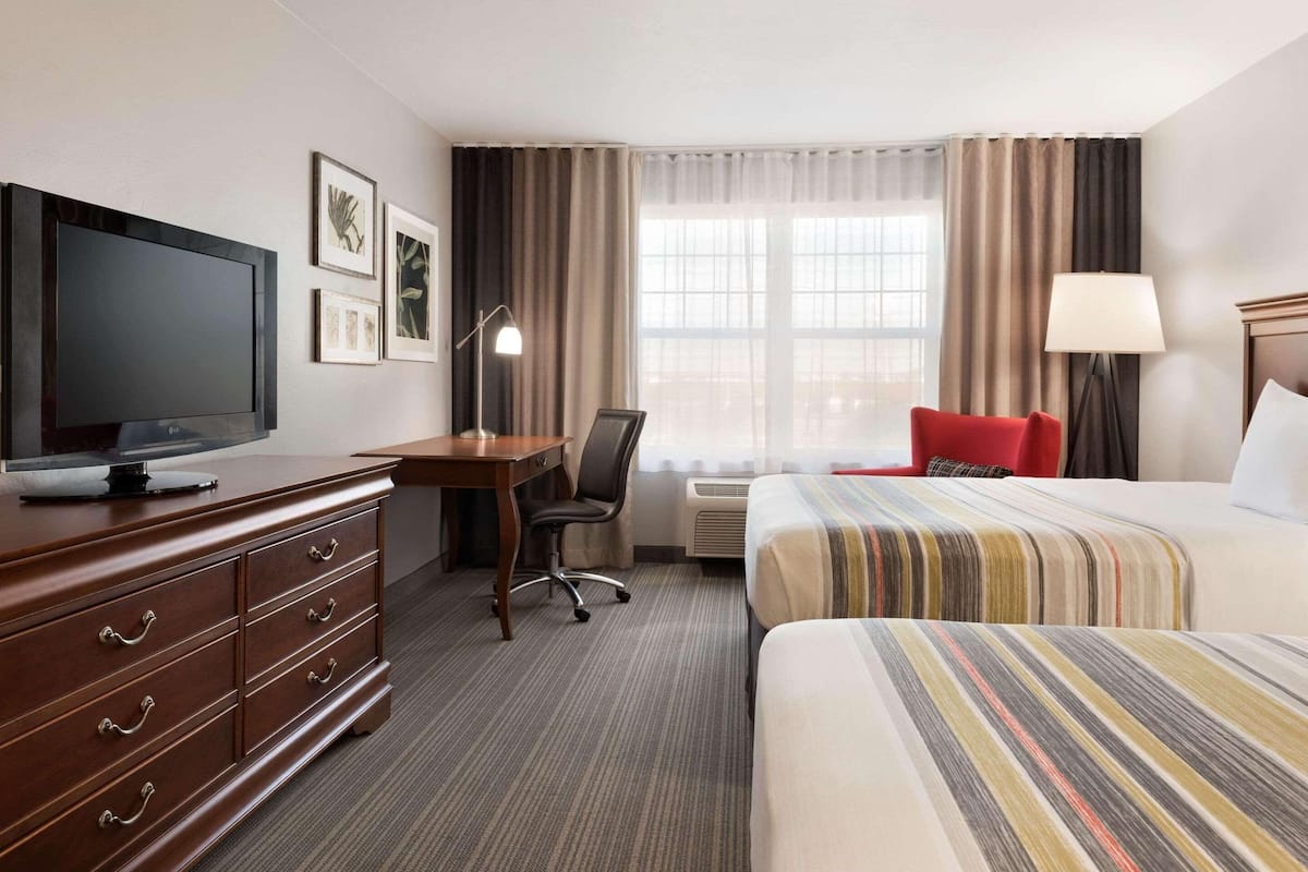 A hotel room with a bed, a desk with a television, a chair, a dresser, and a window with curtains.