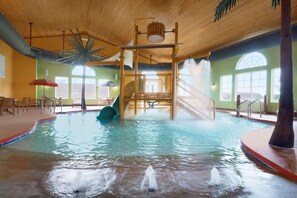 An indoor swimming pool with a slide, a water fountain, and a wooden play structure.