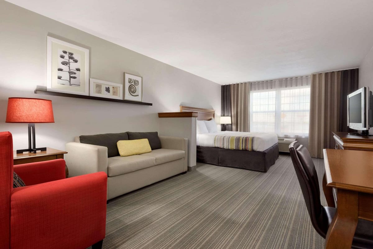 A hotel room with a sofa, a bed, a desk, a TV, and a lamp.