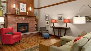 A living room with a brick fireplace, a red armchair, a grey armchair, a beige sofa, and a wooden coffee table. - Country Inn & Suites by Radisson, Appleton North, WI (Little Chute)