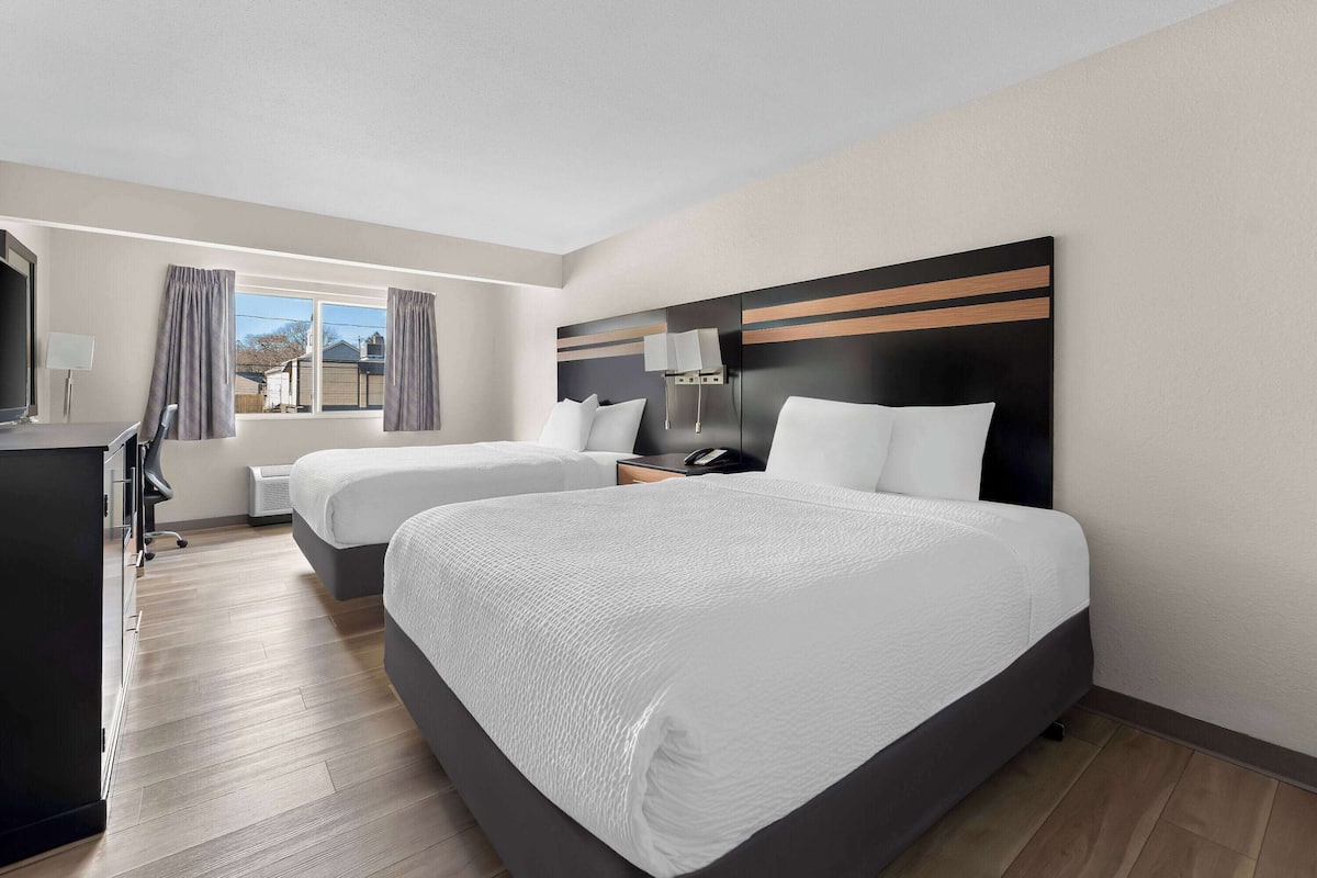 Ein Hotelzimmer mit zwei Betten, einem Schreibtisch, einem Stuhl und einem Fenster mit Vorhängen.