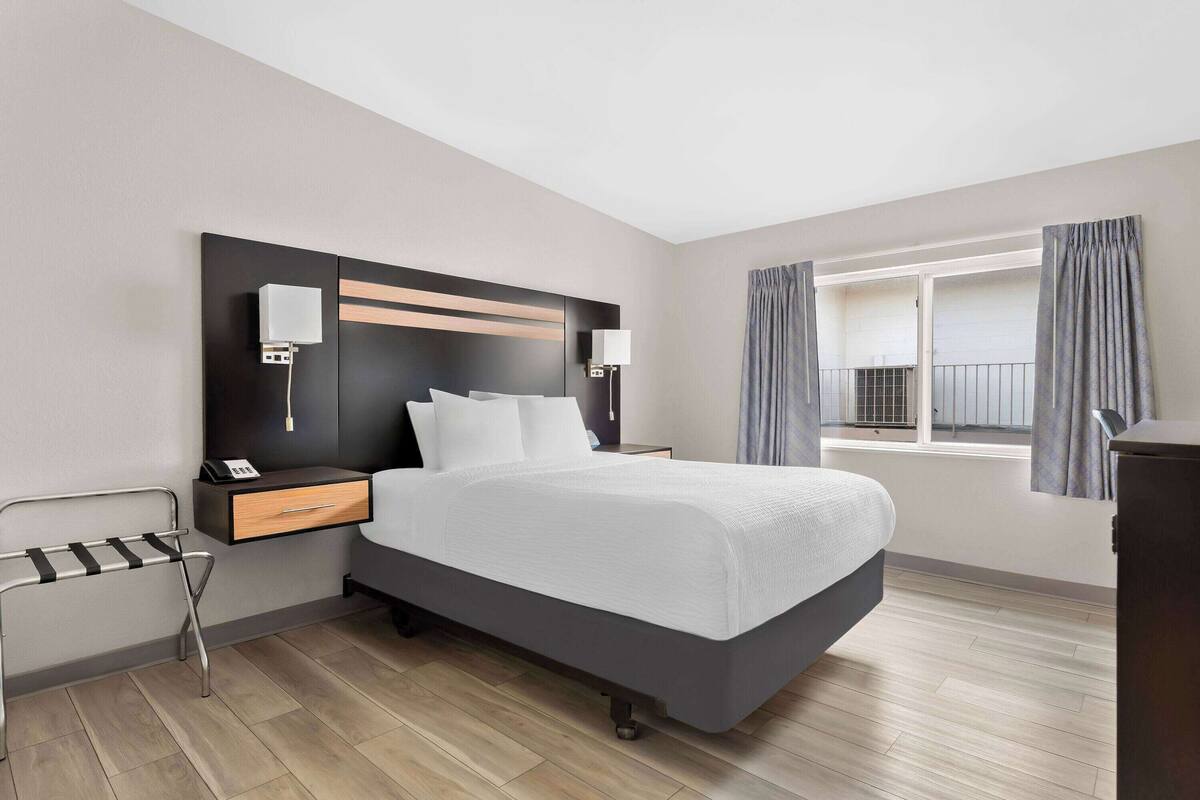Ein modernes Hotelzimmer mit einem großen Bett, Nachttischen, einem Schreibtisch und einem Fenster mit Vorhängen.