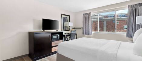 A hotel room with a large bed, a desk with a chair, a television, and a window with curtains.