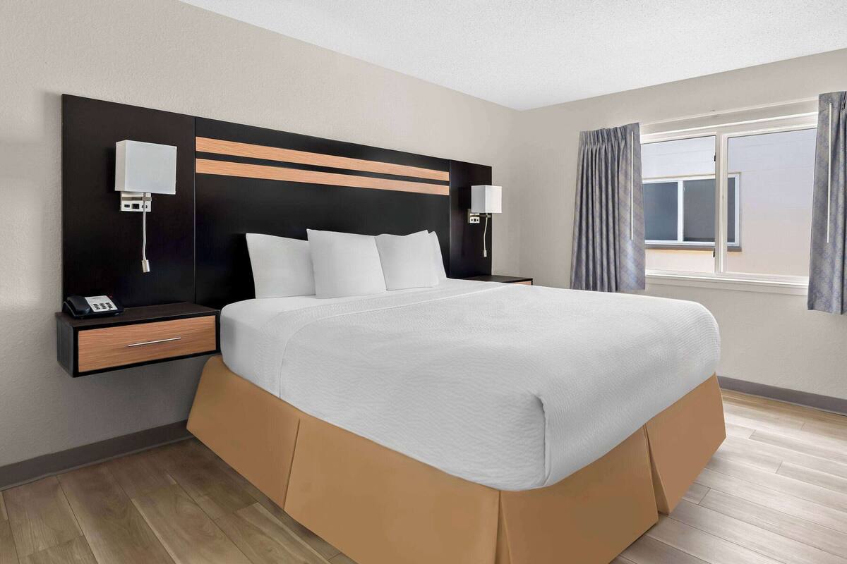 Ein modernes Hotelzimmer mit einem großen Bett, Nachttischen, einem Fenster mit Vorhängen.