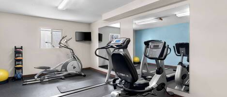 Une salle de sport équipée de tapis de course, de vélos elliptiques et de ballons d’exercice.