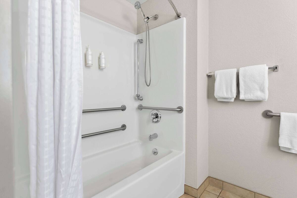 Ein modernes Badezimmer mit einer Duschkabine, Haltegriffen und weißen Handtüchern an einem Handtuchhalter.