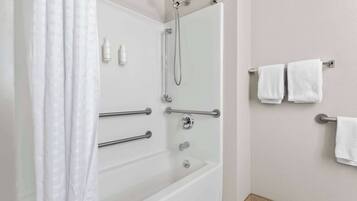 Un baño moderno con ducha envuelta en vidrio, barras de apoyo y toallas blancas en un perchero.