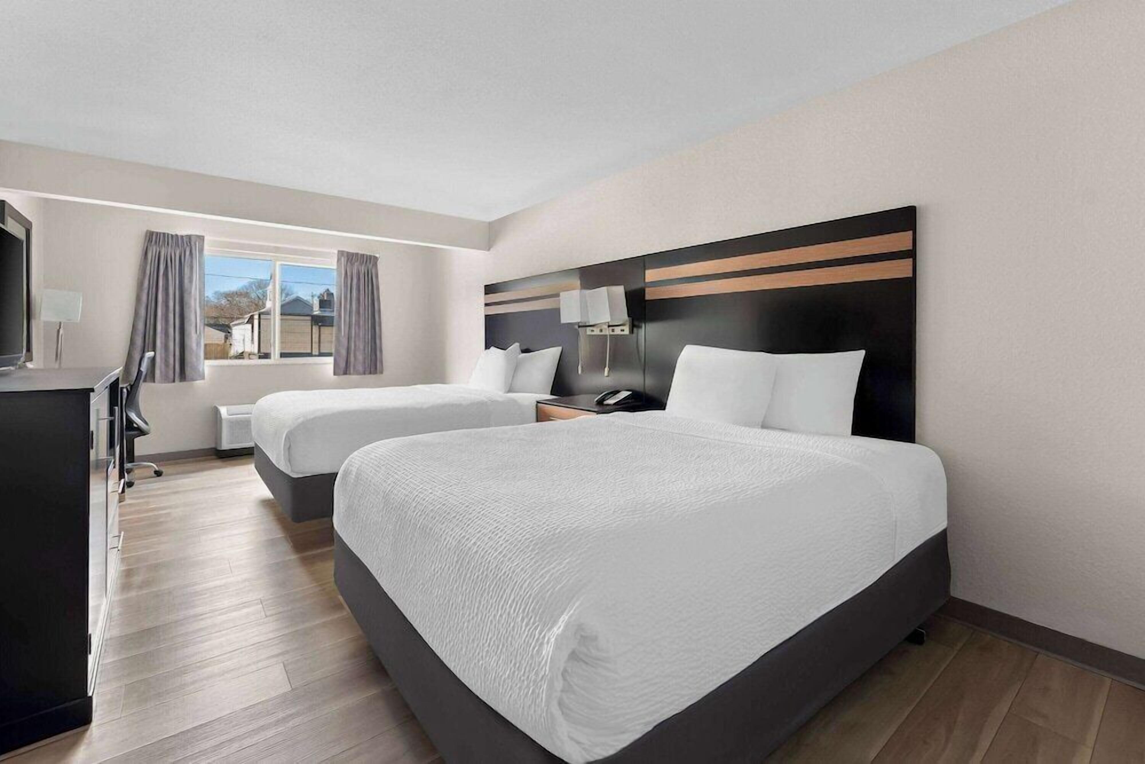 A hotel room with two beds, a desk, a chair, a TV, and a window with curtains.