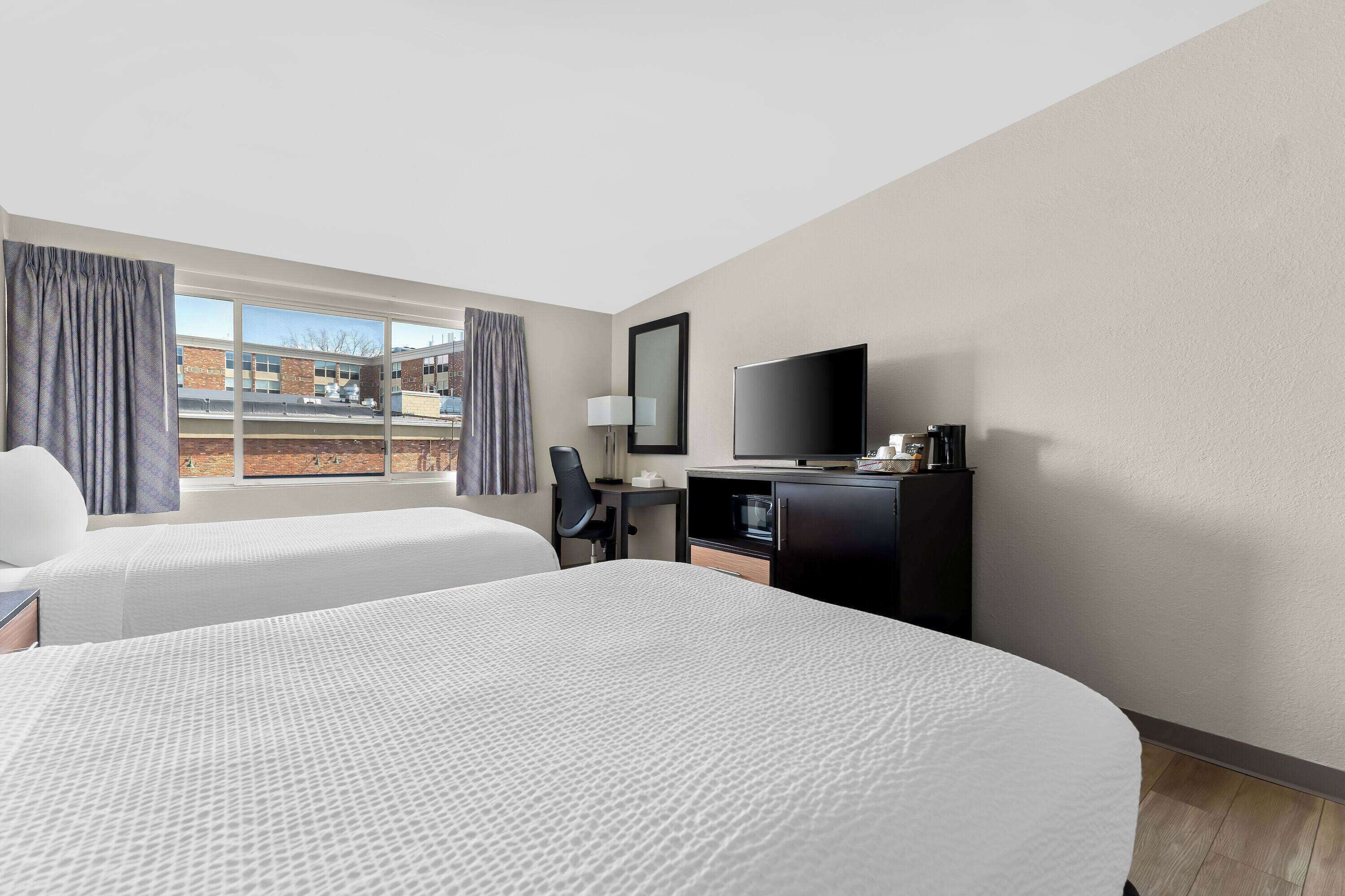 Habitación de hotel con dos camas, un escritorio con televisor y una ventana con cortinas.