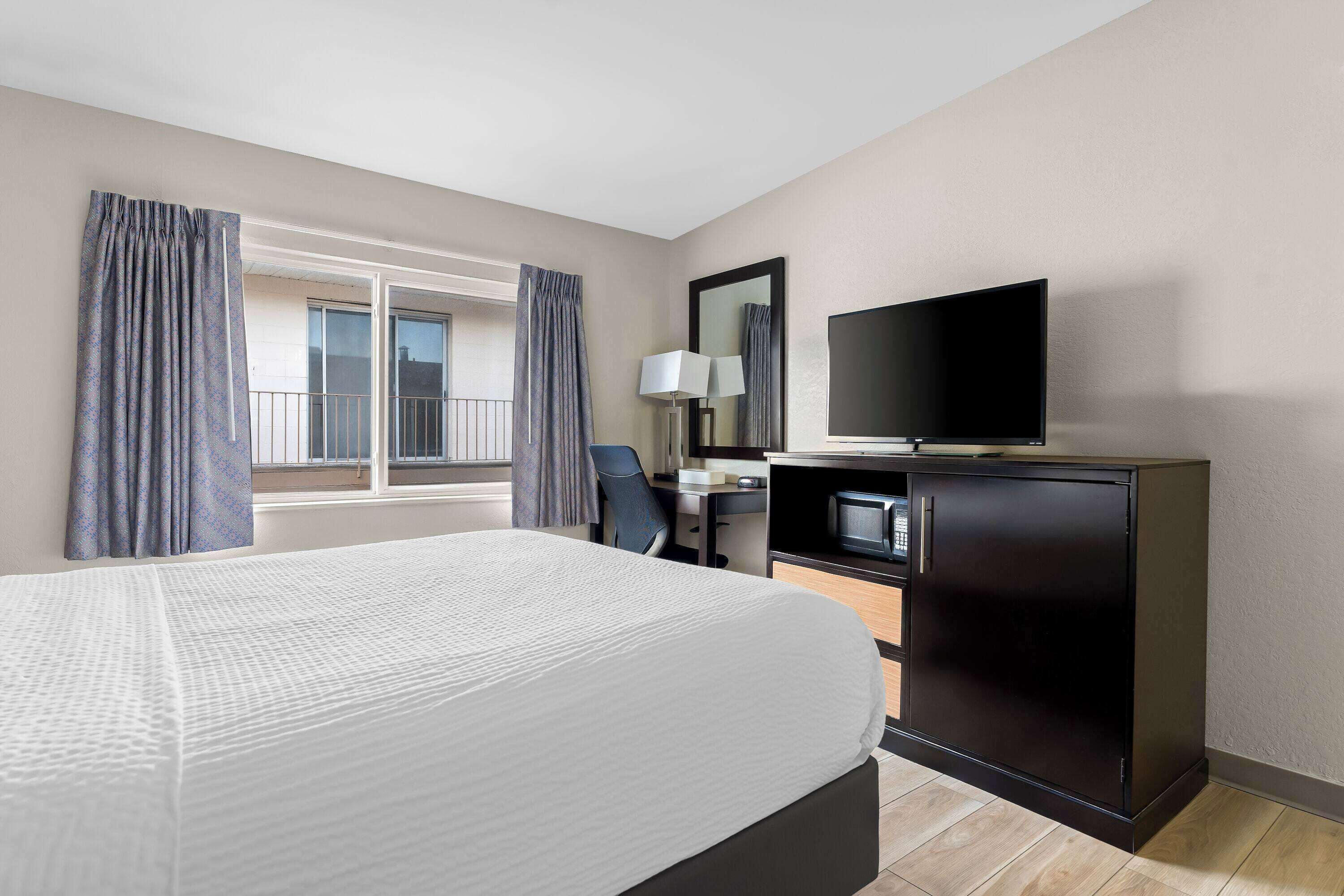 Una habitación de hotel con una cama, un escritorio con computadora, un televisor y una ventana con cortinas.