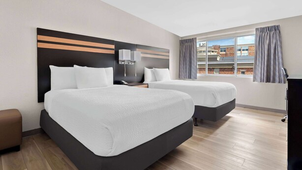 Een hotelkamer met twee bedden, een nachtkastje, een lamp en een raam met gordijnen.