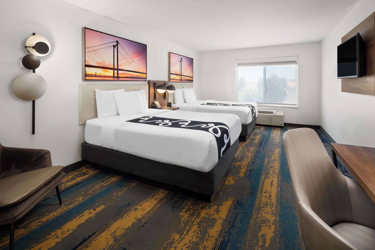 A hotel room with two beds, a sofa, a TV, and artwork on the walls.