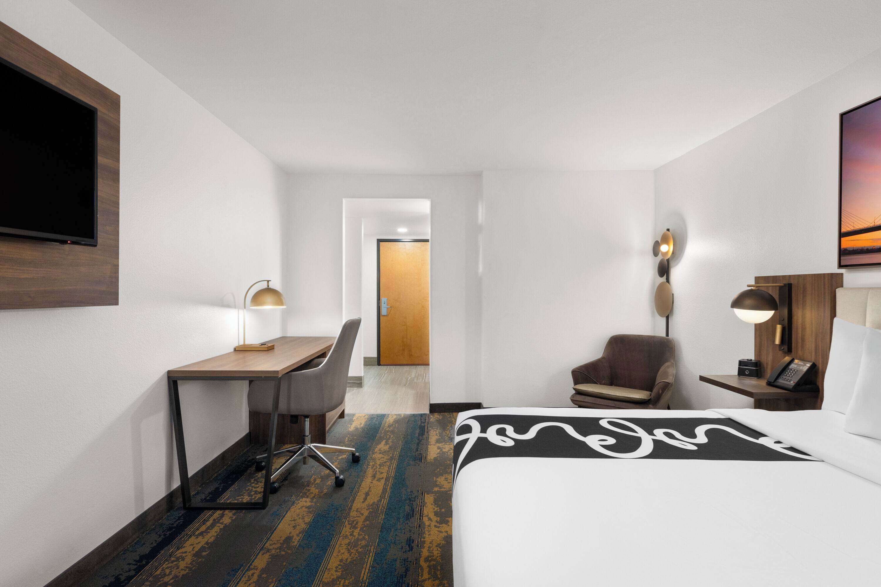 Une chambre d’hôtel équipée d’un lit, d’un bureau, d’une chaise et d’un téléviseur fixé au mur.