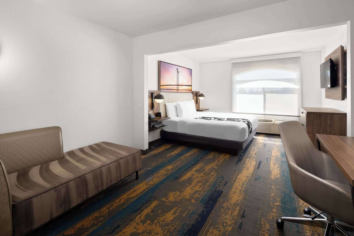 A hotel room with a bed, a sofa, a desk, and a large window.