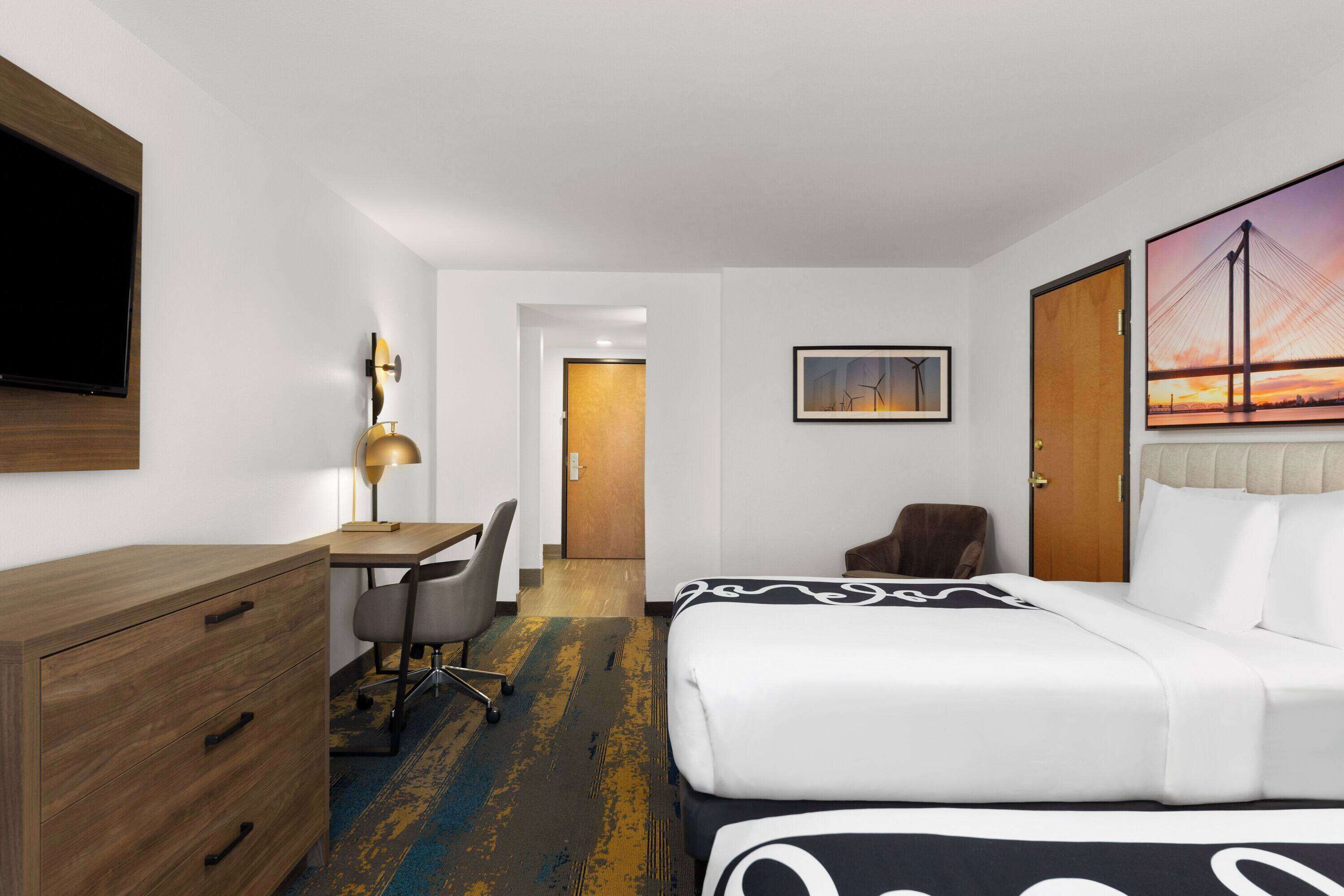 A hotel room with a bed, desk, chair, and a TV mounted on the wall.