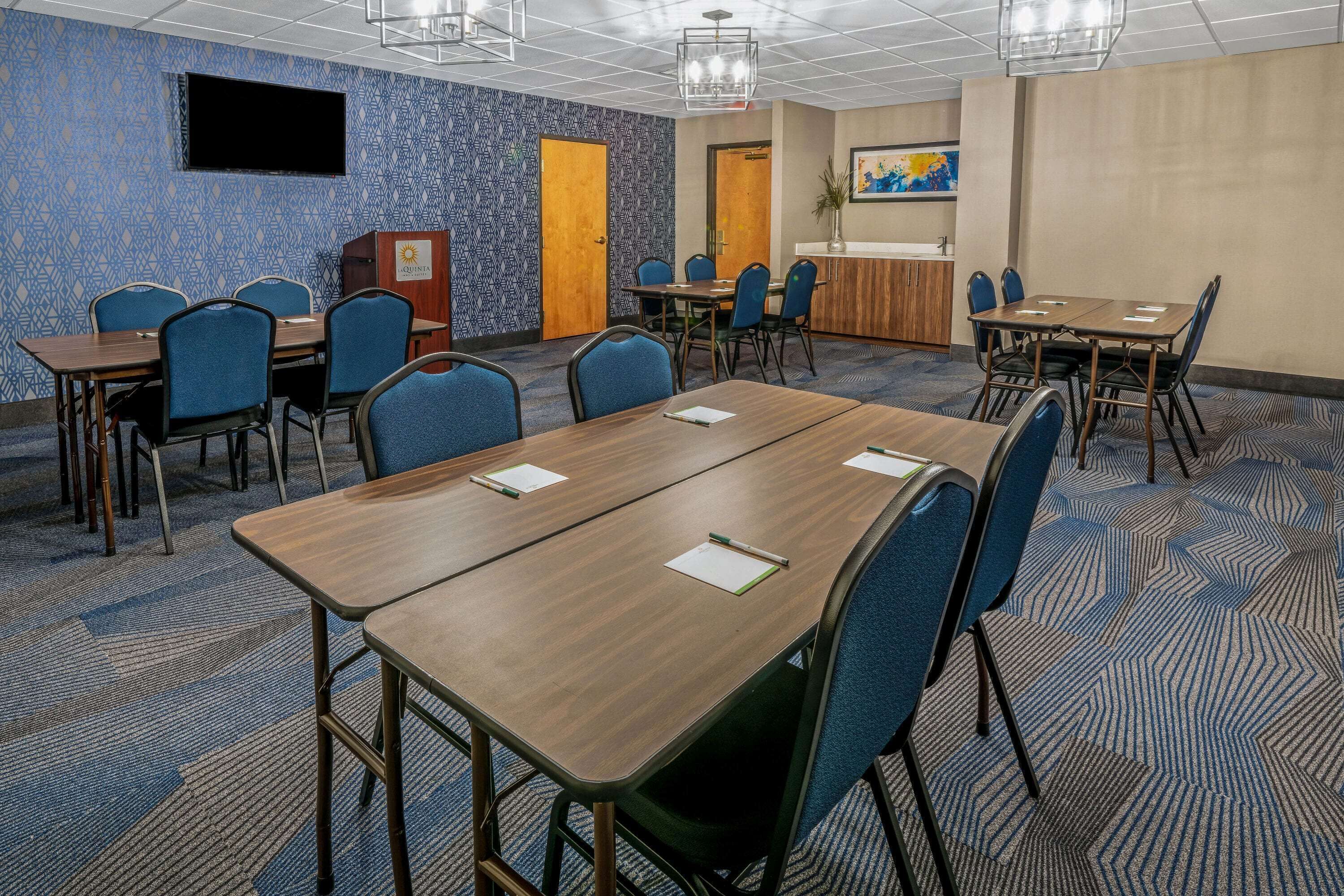Un salón de conferencias con varias mesas y sillas, un atril, una televisión y un cuadro en la pared.