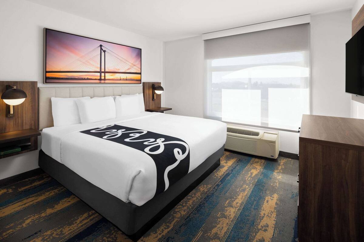 A hotel room with a large bed, a view of a bridge, a flat-screen TV, and a window with a view of the city.