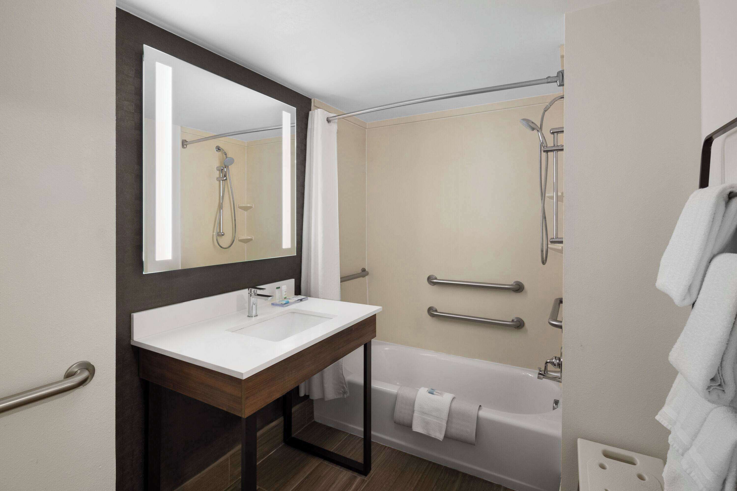 A modern bathroom with a white sink, a large mirror, a bathtub, and a shower area.
