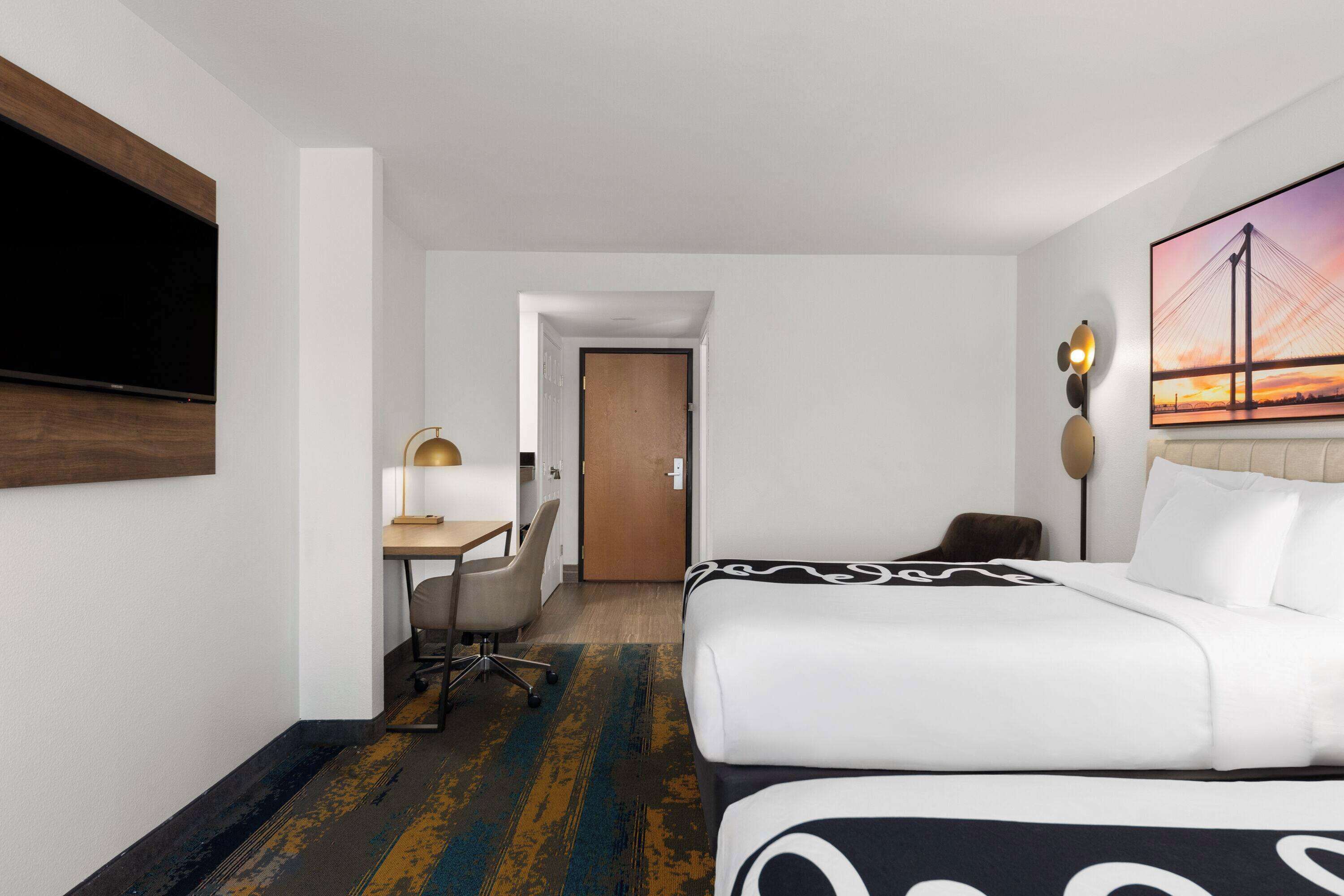 Habitación de hotel con cama, escritorio, silla y un cuadro de un puente.